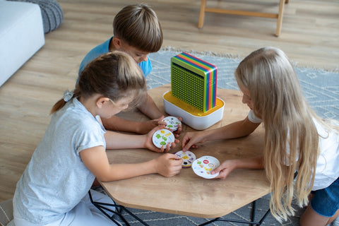 Three children around a table, discussing their paintings and experiences; on the table, SalinoVati's aura in rainbows.