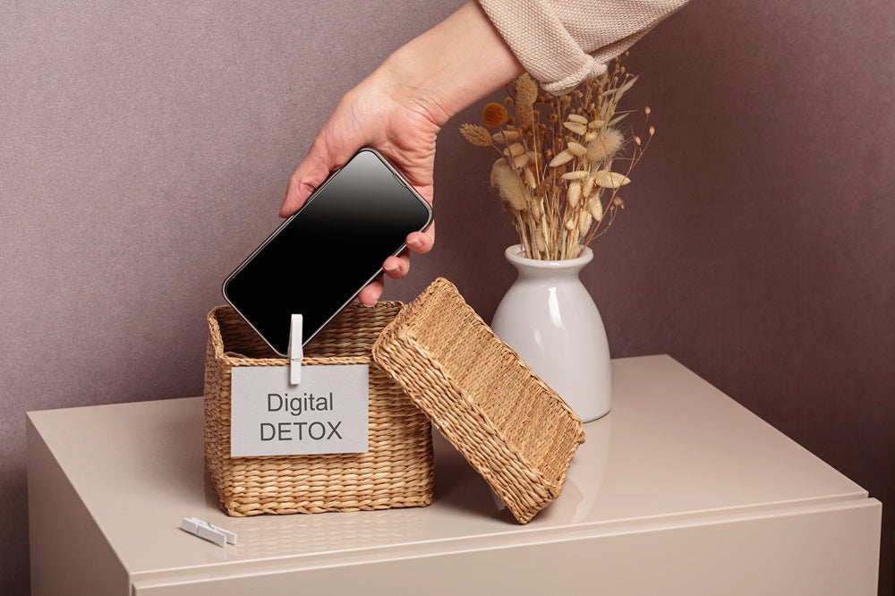 Hand legt ein Smartphone in einen Korb mit der Aufschrift Digital Detox